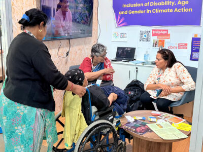 Prof Asha Hans at Disability Caucus booth, COP 30, speaking with a woman.