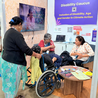 Prof Asha Hans at Disability Caucus booth, COP 30, speaking with a woman.